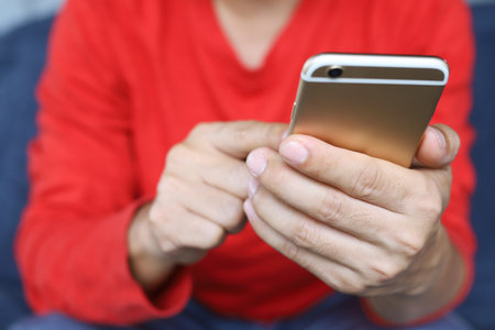 close up hand young male casual wear Red shirt using on cell phone during rest on sofa. sitting in watching message on mobile phone during break relax.の写真素材