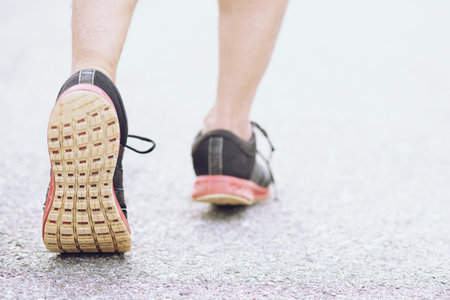 Sportsman runner feet running on road. close up on shoe behind of a man running fitness jogging workout. wellness exercise concept.の写真素材