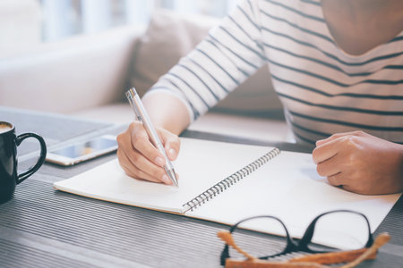 Woman freelancer working hand writing journal on small notebook notepad in coffee shop using with...
