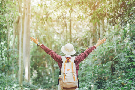 Freedom Tourist traveler young girl with backpack standing with raised arms and enjoying a beautiful nature on forest. Hiker looking sunlight amazing in trip. wanderlust travel concept.の写真素材