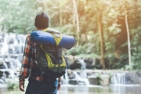 Traveling tourist man Backpack looking at amazing tropical mountains forest waterfall river. Travel Camping Hiking Journey holiday Concept. space for text, atmospheric moment summer vacations outdoor.の写真素材