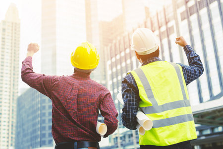 Close up back view of engineering male two construction worker holding safety yellow helmet and white helmet with wear reflective clothing for the safety of the work operation. outdoor of building.の写真素材