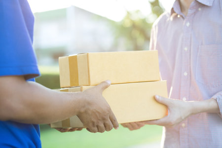parcel delivery man of a package through a service. and close up hand customer accepting a delivery of boxes from delivery man postal.の写真素材