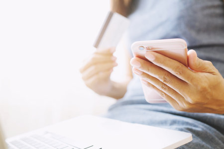 female hands holding credit card and using phone and computer laptop. Online shopping purchase Sell or Payment.の写真素材