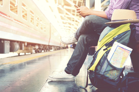 Young man traveler with backpack and hat use phone with waiting for train. Travel conceptの写真素材