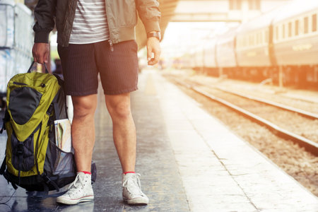 Young man travel alone by train hipster Legs wearing shorts and shoes hold backpack with map on the is a train station,Image for travel and freedom concept.の写真素材