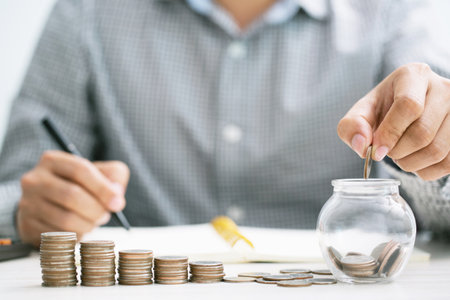 close up hand business man accounting with savings money coins stacked row with hand putting coins in jug glass. concept Write Finance accounting.の写真素材