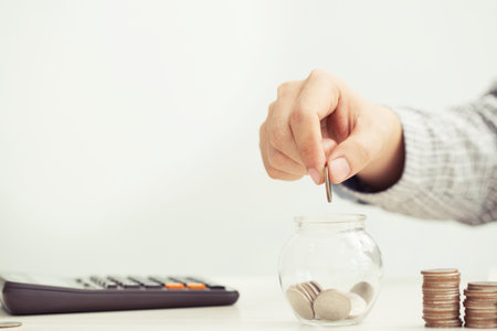 close up hand business man accounting calculator with savings money coins stacked row with hand putting coins in jug glass. concept Write Finance accounting.の写真素材