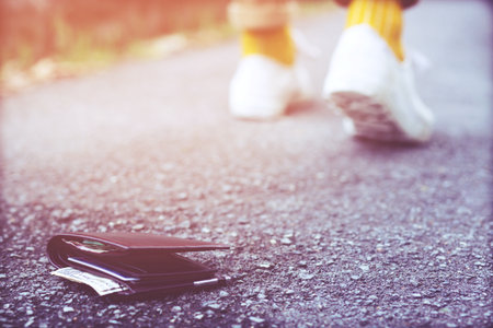 people young hipster had lost leather wallet with money on the street. Close-up of wallet lying on the road concrete sidewalk in during the trip to travel. with filter Tones retro vintage warm effect.の写真素材