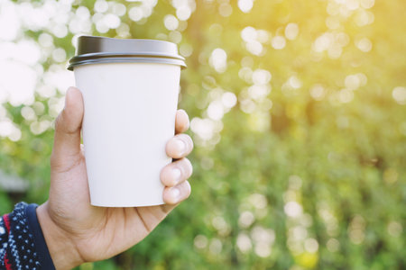 people man hand holding paper cup of take away drinking coffee on natural morning sunlight. space Place for your text or logo.の写真素材