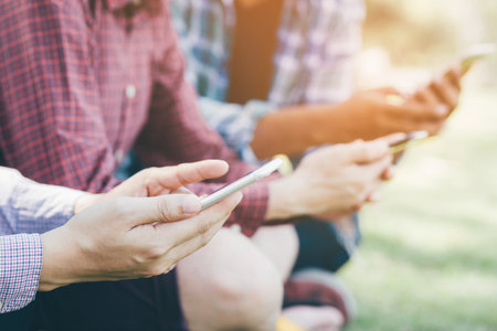 Young male friends group sit meeting exchange call mobile smart phone number and send message in outdoor public park.の写真素材