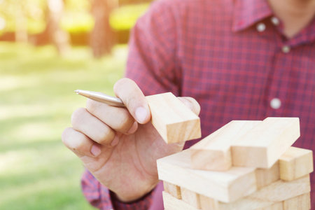 Game jenga, Close up of people man's hand holding pen playing take one block wood stack game on the tower in outdoor, concept Planning risk and strategy in businessman and engineer.の写真素材