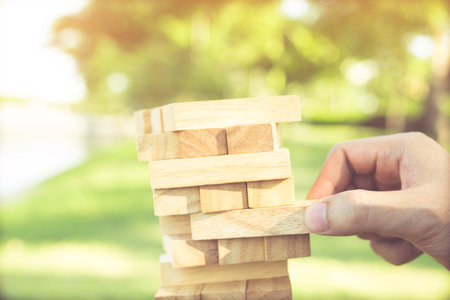 Game jenga, Close up of people man's hand playing take one block wood stack game on the tower in outdoor, concept Planning risk and strategy in businessman and engineer.の写真素材