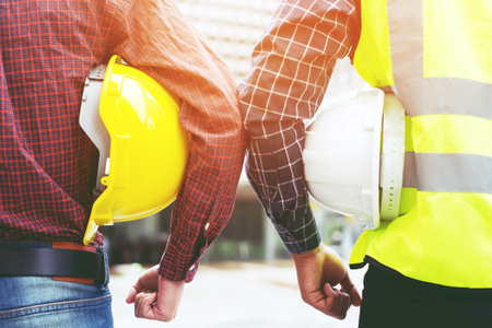 Close up back view of engineering male two construction worker holding safety yellow helmet and white helmet with wear reflective clothing for the safety of the work operation. outdoor of building.の写真素材