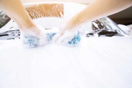 2 hands hold with blue sponge clean front hood the car wash.の写真素材
