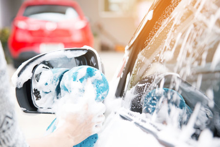 Female hand with blue sponge clean washing car side mirror. concept car wash cleaning.の写真素材