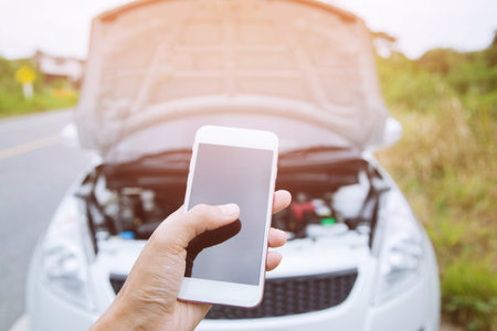broken car on the road and smart phone, woman hand holding mobile smart phone,cellphone Contact ask for help car technician repairing the car in garage.の写真素材