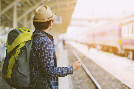 Young man traveler with Wearing sunglasses backpack and hat looking the map with waiting for train. Travel concept.の写真素材