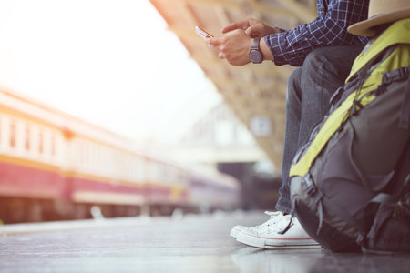 Young man traveler with Wearing sunglasses backpack and hat looking the map with waiting for train. Travel concept.の写真素材