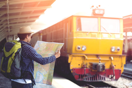 Young man traveler with Wearing sunglasses backpack and hat looking the map with waiting for train. Travel concept.の写真素材