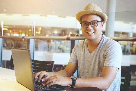 young man hipster working on his laptop in a coffee shop. rear view of business man hands busy using laptop at office desk or young male student typing on computer sitting at wooden table.の写真素材
