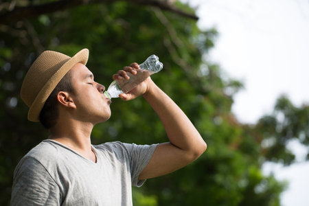 Young asian man guy thirsty Drink bottled water in parks Sunlight Outdoors.の写真素材
