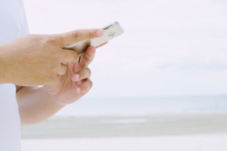 Close up hand young man cell phone man using smartphone find the signal for chatting, and sending text message in internet and mobile . the beach sea backgroundの写真素材