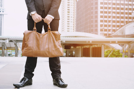 Closeup of a young businessman entrepreneur with boots and a briefcase stand office frontの写真素材