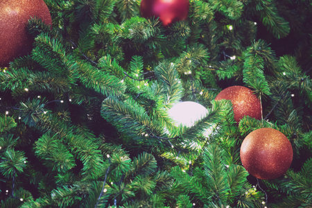Closeup of red bauble hanging from a decorated christmas tree on blurred of lights with decorated tree, sparkling and bokeh background. copy space for your text.の写真素材