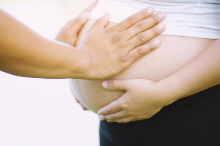 The husband holds the pregnant wife's belly. New mom Pregnant woman in white underwear. Young woman expecting a baby Stand in the outdoors.の写真素材