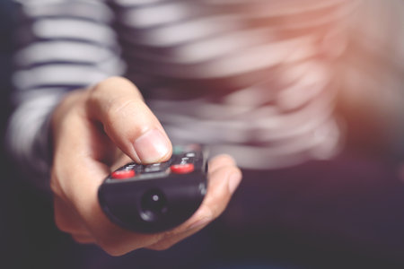 close up Television remote control in casual man hands pointing to tv set and turning it on or off. select channel watching tv on his sofa at home in the living room relax.の写真素材