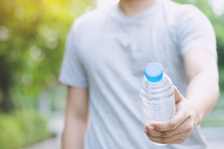 young man Hand holding fresh drinking water bottle from a plastic in the park.