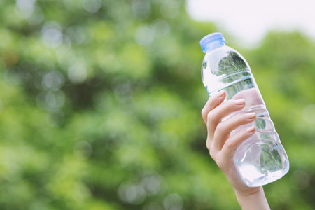 close up young woman hand holding fresh drinking water bottle from a plastic in the park.