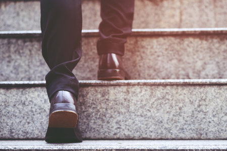 modern businessman hand holding briefcase beside working close up legs walking up the stairs in...
