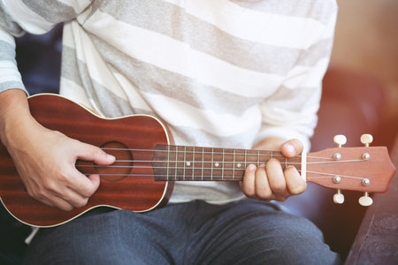 Closeup of young man hands playing acoustic guitar ukulele at the sofa sit Enjoy living room.の写真素材