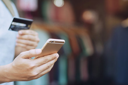 young male hand holding credit card and using mobile smart phone standing in front of the clothing shop store of the T shirt. Online shopping purchase sell or payment. money expenses finance concept.の写真素材