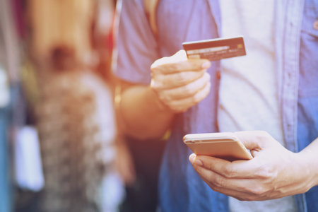 Close up young man hands holding paying with credit card and using cell, smart phone for online shopping Instead of using money Standing in front of a clothing shop store.の写真素材