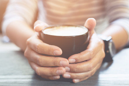 women hands holding a black cup of hot ready to drink on wooden table in cafe while having coffee.の写真素材