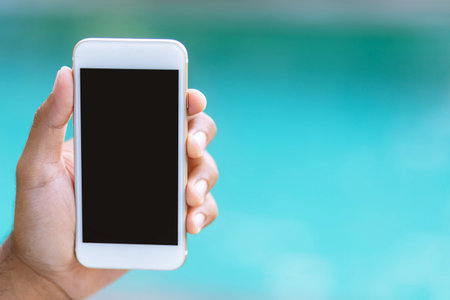 close up people man of hand holding white mobile smart phone on the beautiful blur the background of the water sea. with blank empty screen. empty space for text. Technology and travel holiday conceptの写真素材