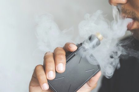 photo portrait young man with beard hold and smoking his electronic cigarette blowing a stream of...
