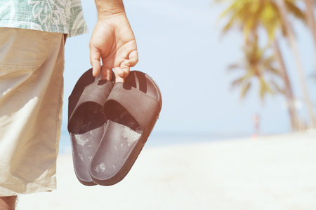 slipper of foot in sandals shoes and Blue ocean wave water distribution on sandy white beach, Sea background.The color of the water and beautifully bright. travel nature holiday summer concept.の写真素材