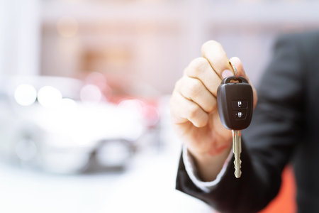 Business man hand holding car key front with car in showroom on background. transport dealership and sales conceptの写真素材