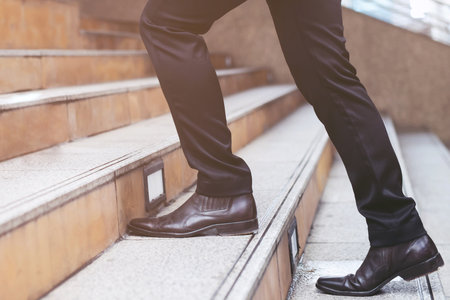 Close up legs shoes of young business man One person walking stepping going up the stairs in modern...