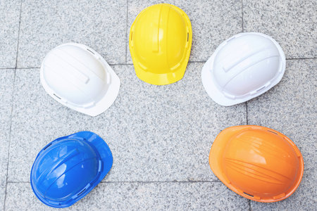 orange, yellow, blue, white hard safety wear helmet hat in the project at construction site building on concrete floor on city. helmet for workman as engineer or worker. concept safety first. top viewの写真素材