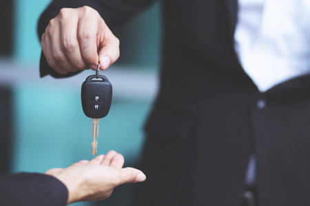 Car key, businessman handing over gives the car key to the other woman on showroom background.の写真素材