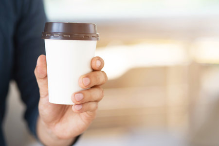 hand holding paper cup of take away drinking coffee on natural morning sunlight. space Place for your text or logo.の写真素材