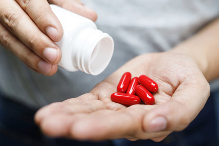 close up man hand holding a medicine, with pours the pills vitamin out of the bottle. Caring for the...