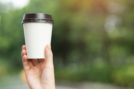 business man hand holding paper cup of take away drinking coffee on natural morning sunlight. space Place for your text or logo.の写真素材