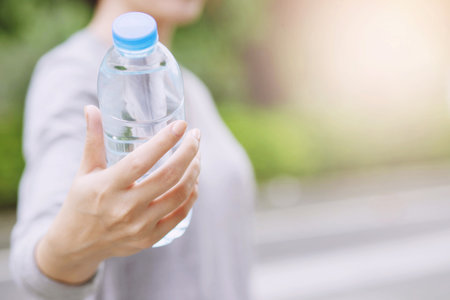 young woman hand holding give fresh drinking water bottle from a plastic in the park Morning...