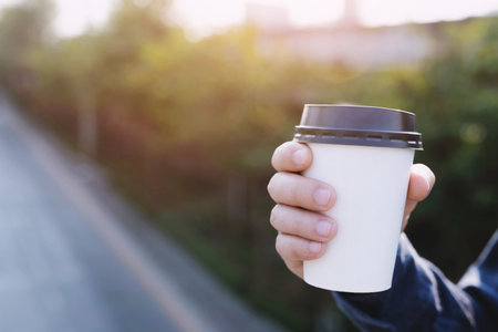 business man hand holding paper cup of take away drinking coffee on natural morning sunlight. space...
